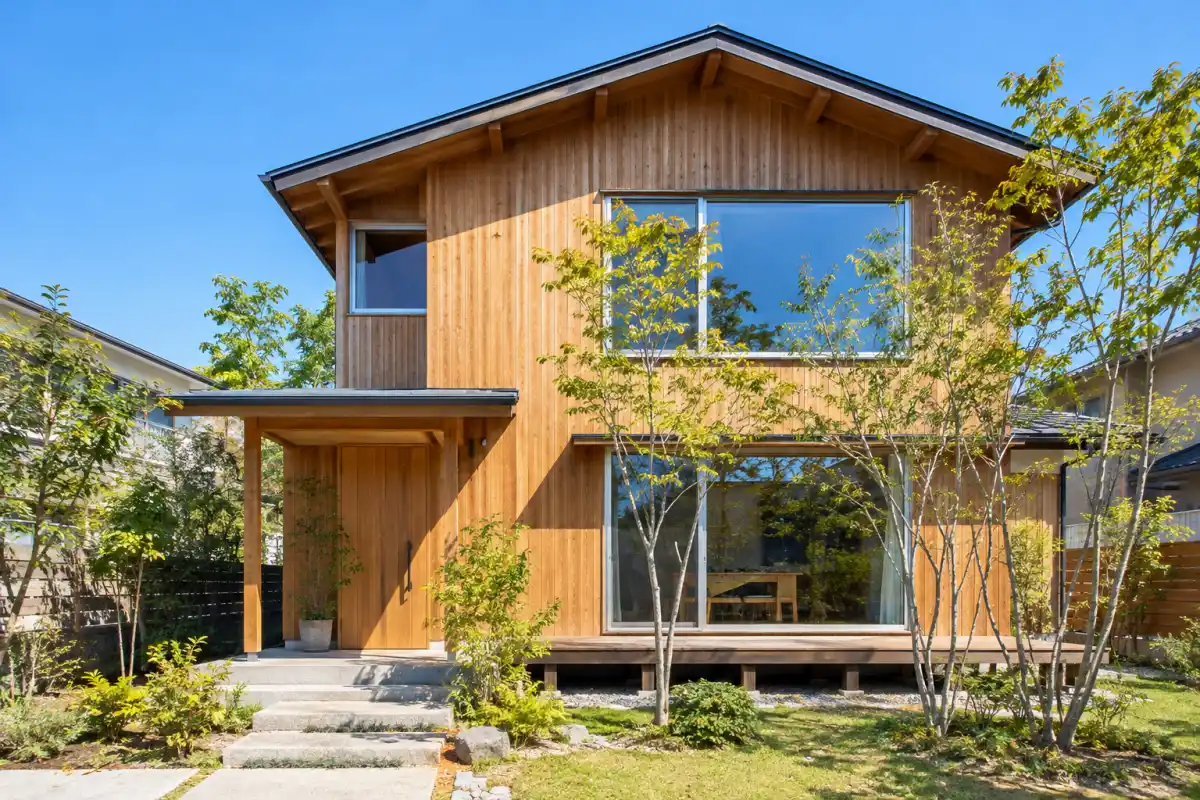 木の外壁の 2 階建ての住まいと、小さな庭の植栽